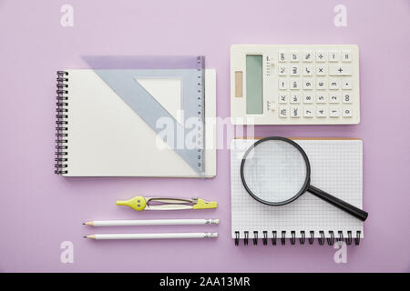 top view of magnifier and ruler triangle on notebooks near calculator and stationery isolated on purple Stock Photo