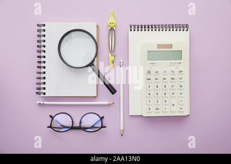 top view of magnifier on notebook near calculator and glasses isolated on purple Stock Photo