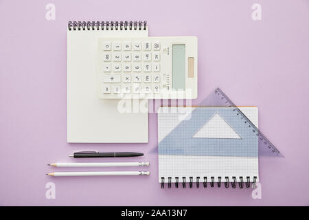 top view of ruler triangle on notebook near calculator and stationery isolated on purple Stock Photo