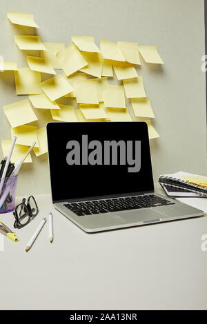 laptop with blank screen near yellow sticky notes and stationery on grey and white Stock Photo