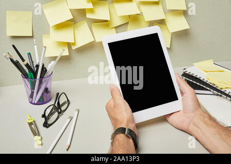 cropped view of man holding digital tablet with blank screen near stationery and notebooks on grey and white Stock Photo