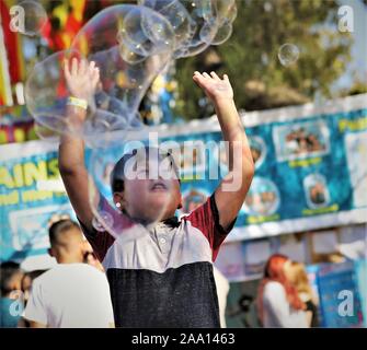 Hispanic Latin Mexican kids, boys and girls, chasing bubbles from fair circus act made with soap and water for public entertainment and family fun Stock Photo