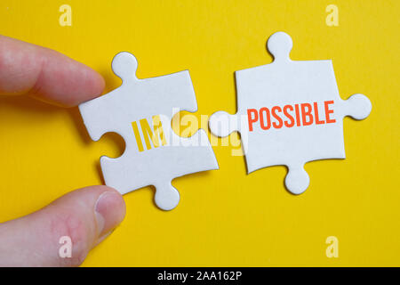 The concept is everything is possible. A piece of the puzzle with the inscription holds the fingers of a man next to another on a yellow background. C Stock Photo