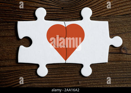 The concept of mutual love. Pieces of a connected white puzzle with red heart on a wooden background. Flat lay. Stock Photo