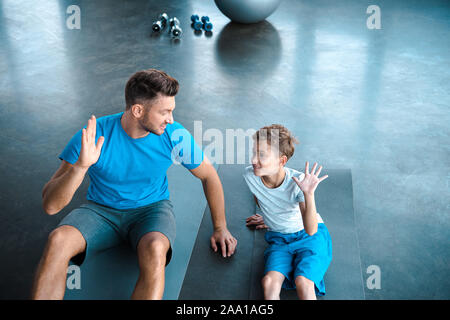 cute kid and father looking at each other while giving high five in gym Stock Photo
