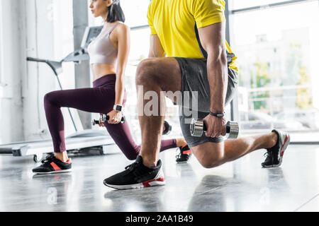 cropped view of sportsman and sportswoman doing lunges with dumbbells in sports center Stock Photo