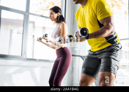 cropped view of sportsman and sportswoman working out with dumbbells in sports center Stock Photo