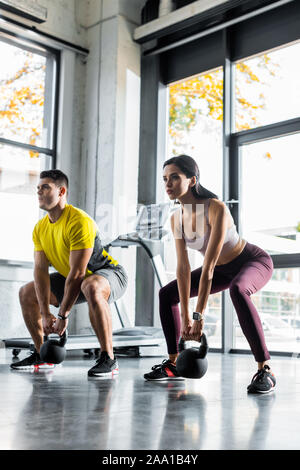 sportsman and sportswoman doing squat with weights in sports center Stock Photo