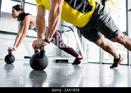 cropped view of sportsman and sportswoman doing plank on weights in sports center Stock Photo