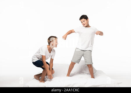 smiling boy squatting on bed near brother imitating boxing isolated on white Stock Photo