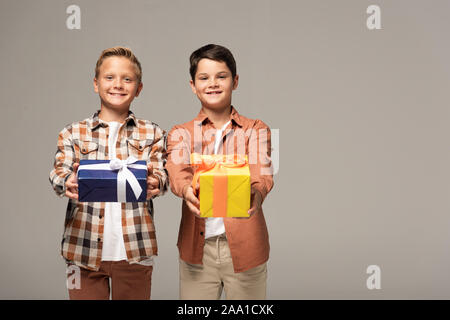 two happy brothers holding blue and yellow gift boxes isolated on grey Stock Photo