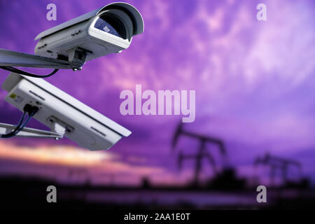 CCTV camera concept with silhouettes of oil well on oil field with nice sunset sky background Stock Photo