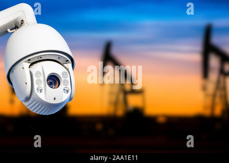 CCTV camera concept with silhouettes of oil well on oil field with nice sunset sky background Stock Photo