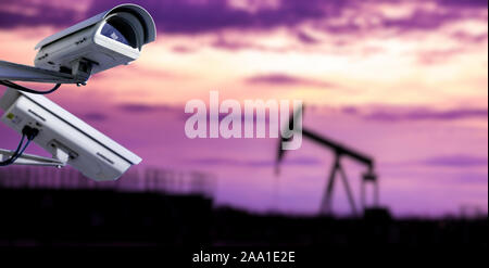 CCTV camera concept with silhouettes of oil well on oil field with nice sunset sky background Stock Photo