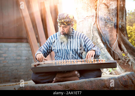 Asian old man playing kecapi with tree background. Kecapi is a ...