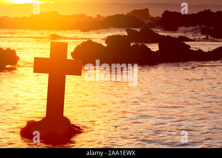 Christian Cross on the beach with a sunset sky background Stock Photo