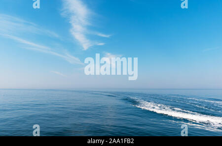 Boat cruising the sea leaving wake on a brilliant sunny day. Beautiful blue sky with light white clouds. Stock Photo