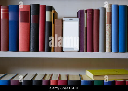 Mobile phone between colourful books in a shelf Stock Photo