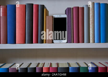 Mobile phone between colourful books in a shelf, front view Stock Photo