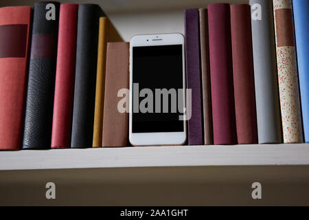 Close up of mobile phone in bookshelf, low angle Stock Photo