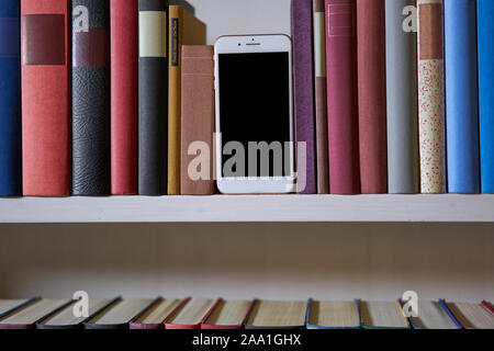 New mobile phone between colourful books in a shelf at home Stock Photo