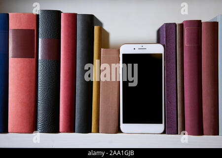 Close up of a mobile phone in colorful bookshelf, standing upright Stock Photo