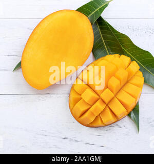 Beautiful chopped ripe mango with green leaves on bright white color wooden background, top view, flat lay, copy space. Tropical fruit design concept. Stock Photo