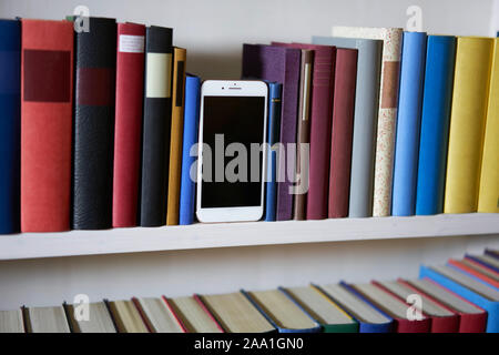 Mobile phone in colorful and accurate bookshelf, standing upright Stock Photo