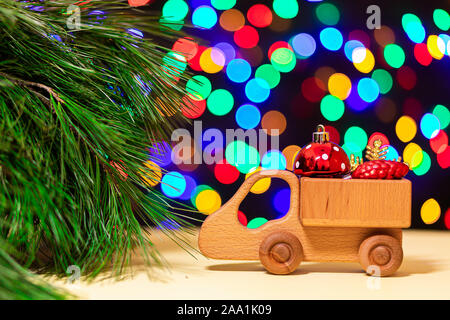 a close-up of a wooden truck brought red Christmas balls to a Christmas tree on the background of many colorful lights. Picture for New Year's design, Stock Photo