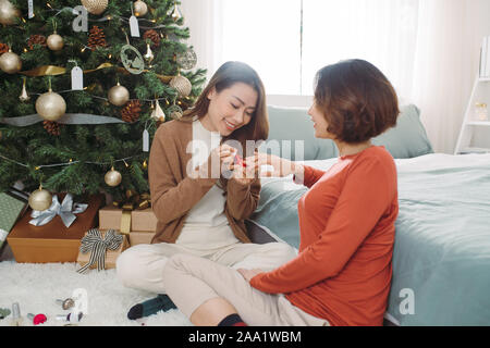 Two young girlfriends polishing nails in living room at home during Holiday. Christmas time. Stock Photo