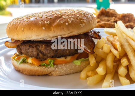 Jumbo beef burger with bacon, cheese, lettuce, tomato and french fries. Cooked food on table concept. Stock Photo