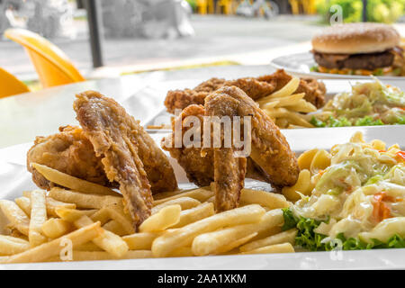 Close-up detailed view of two pieces of fried chicken wings, french fries, Mac & Cheese and fresh coleslaw on top of green lettuce Stock Photo