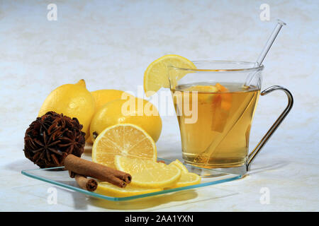 Eine Tasse Tee  mit Zitronen, Nelken  und Zimtstangen auf einem Glasteller / A cup of tea with lemon, cloves and cinnamon sticks on a glas plate Stock Photo