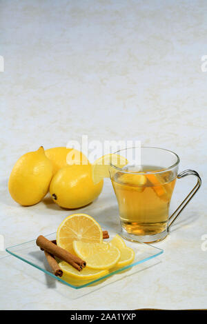 Eine Tasse Tee  mit Zitronen  und Zimtstangen auf einem Glasteller / A cup of tea with lemon and cinnamon sticks Stock Photo