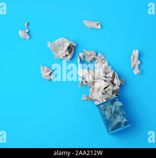 overturned blue metal basket with crumpled pieces of paper, concept of recycling and pollution, blue background Stock Photo