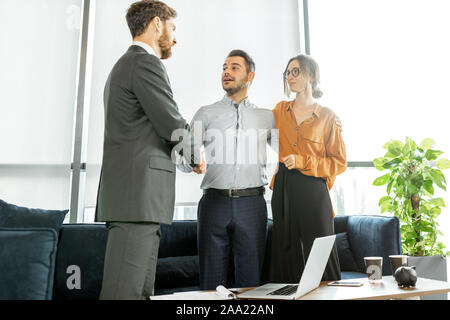 Young and happy couple having a deal, shaking hands with financial consultant or real estate agent at the luxury office Stock Photo