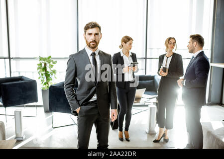 Portrait of a handsome white collar worker standing in front of business team at the luxurious office Stock Photo