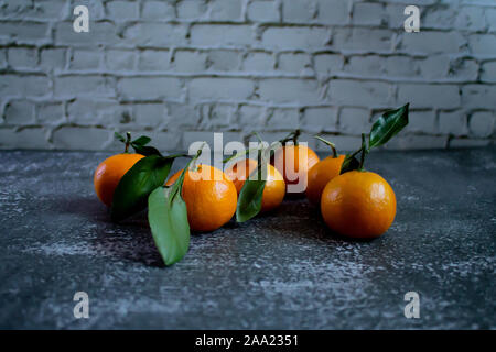 Gray concrete background with a brick wall, tangerines with leaves and twigs view from the top. New Year, in the style of health. Stock Photo