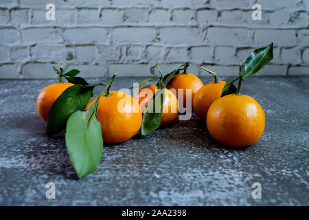 Gray concrete background with a brick wall, tangerines with leaves and twigs view from the top. New Year, in the style of health. Stock Photo