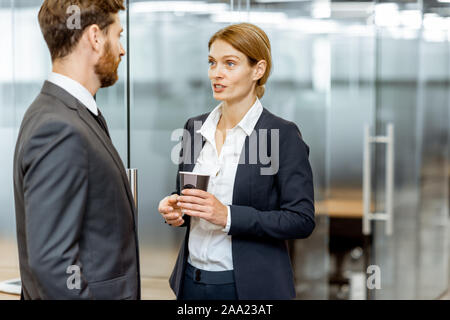 Business man and woman meeting in the hallway of the modern office building, white-collar workers having informal discussion Stock Photo