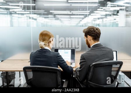 Two white-collar employees working on the laptop at the working place in the finance department of a large corporation, backside view Stock Photo
