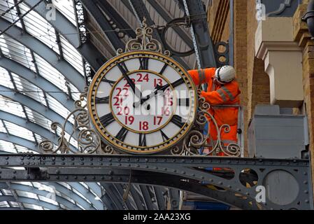 A clock repairer attends to maintenance on the large station clock above the platform at London Kings Cross Station Stock Photo