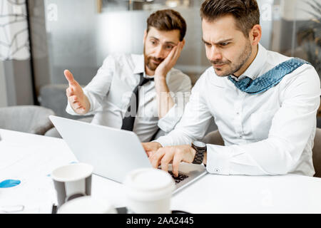 Two exhausted and tired employees hard working with laptop in the office, having problems and no time to finish their work Stock Photo
