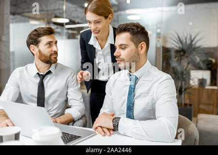 Team leader helping two male exhausted employees to do some work on a laptop in the office Stock Photo