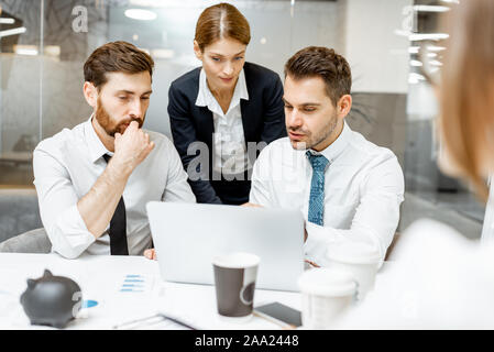 Team leader helping two male exhausted employees to do some work on a laptop in the office Stock Photo