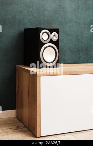 One modern black audio speaker system in interior on wooden desk near the dark green wall. Vertical image Stock Photo