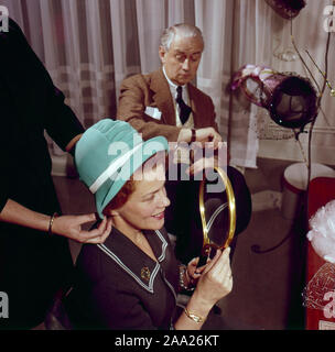 Trying out hats in the 1950s. A woman is trying hats while a man is sitting and looking at the time looking bored. He is humourist Erik Zetterström and she is Sickan Carlsson, actress. Sweden 1950s Stock Photo