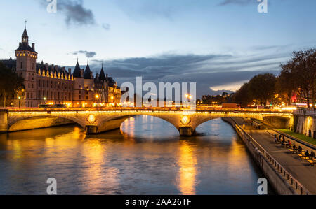 Stone bridge Pont au Change in Paris at the dusk. On the left are towers of Conciergerie, on right northern bank of river Seine Stock Photo