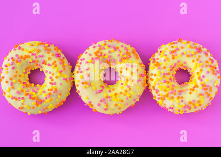 Three yellow round donuts with a hole on a pink background. Top view. Funny mood concept. Laconic food design. Stock Photo