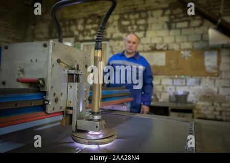 Belarus, the city of Gomil, April 30, 2019. Ventilation pipe factory. Metal cutting machine on the background of the worker. Stock Photo